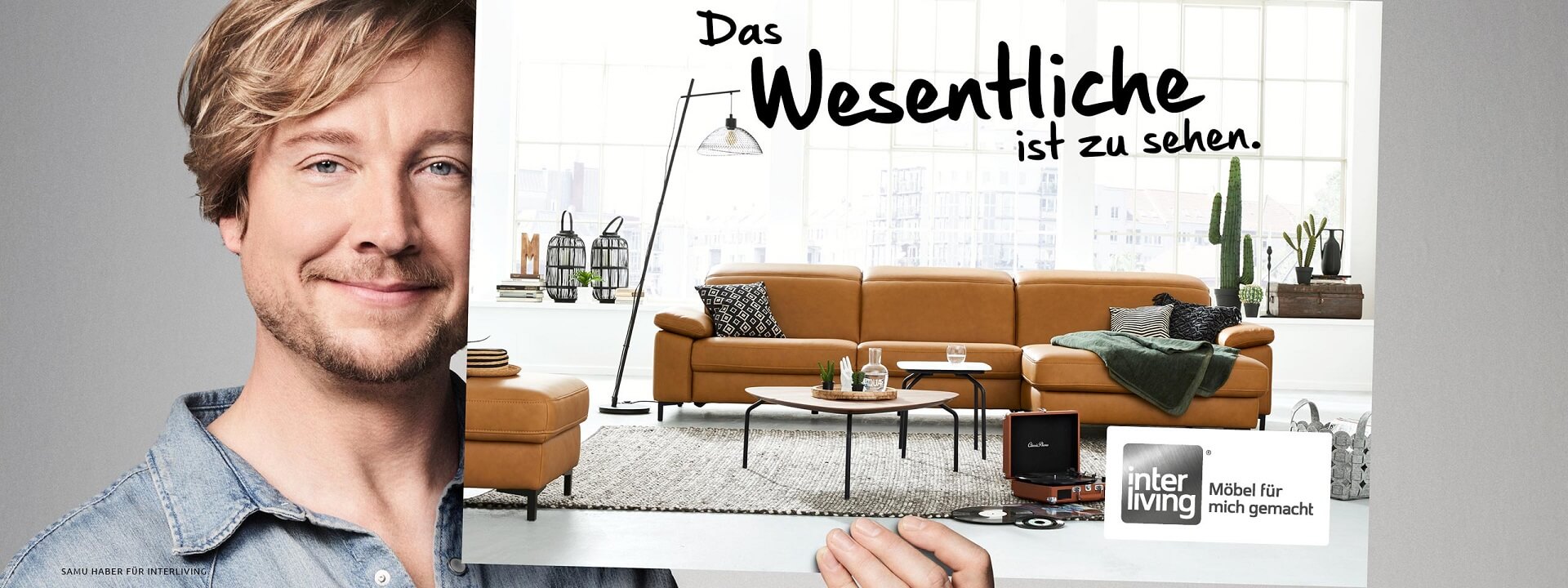 Werbemotiv mit Samu Haber, der ein große bild, darauf ist ein Sofa abgebildet und der Spruch: "Das Wesentliche ist zu sehen".