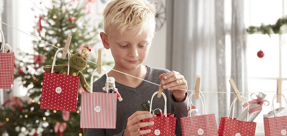 Ein Junge öffnet einen Adventskalender aus Papiertäschchen, die mit wäscheklammern an einer Schnur aufgehängt wurden.